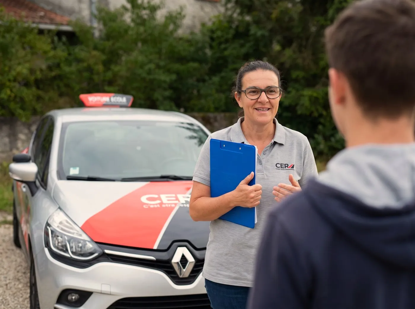 Véronique, enseignante, évalue un élève devant la voiture-école